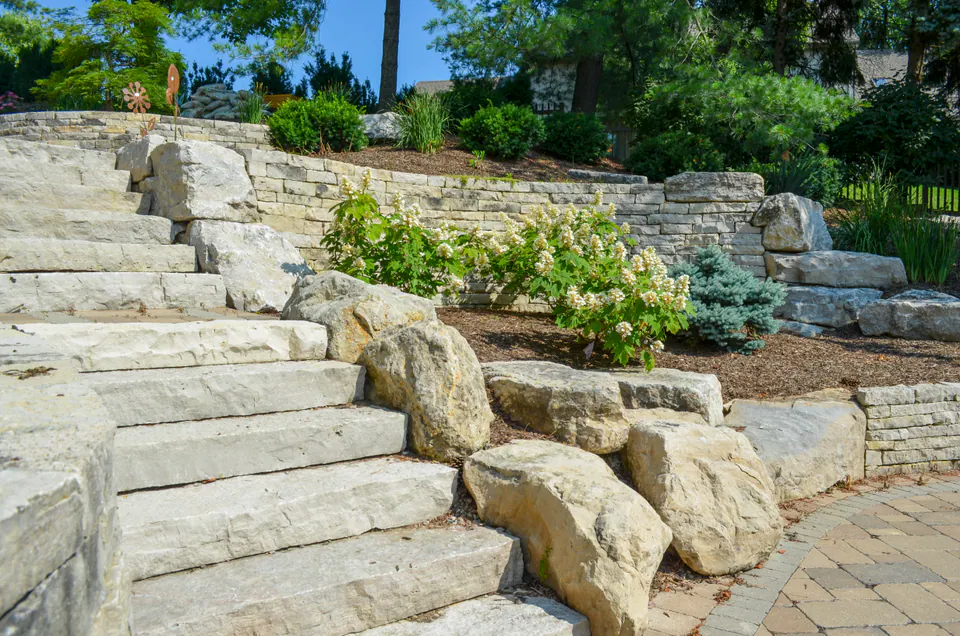 Limestone terraced retaining walls with natural stone steps, boulders, paver patio, hydrangea, and evergreen planting